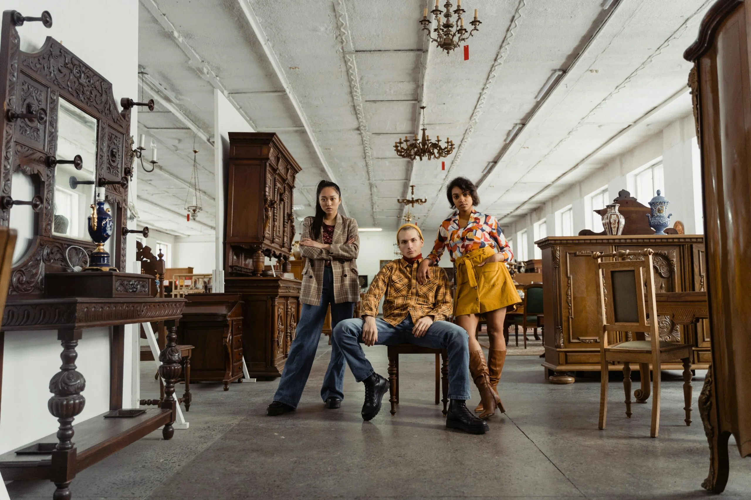 Stylish young adults posing amidst vintage furniture in a spacious warehouse setting.